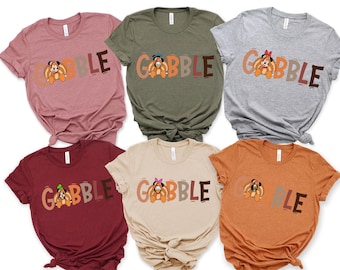 May include: A collection of six short-sleeved t-shirts in various colors, each featuring the word "GOBBLE" in colorful letters with a cartoon turkey character. The shirts are made of soft material and are suitable for casual wear.