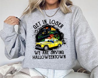 May include: A light gray sweatshirt with a Halloween-themed graphic. The graphic features a yellow taxi cab with a pumpkin driver, a haunted house, and the text "GET IN LOSER WE ARE SAVING HALLOWEENTOWN."