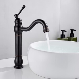 May include: A black and bronze-toned bathroom tap with a curved spout, water flowing into a white, round sink. The tap has a decorative handle and a vintage design. Two green soap dispensers are in the background.
