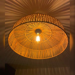 May include: A circular pendant light, woven from orange-toned rope or twine. The light fitting has a central bulb, casting a warm glow. The design is intricate, with the light's rays creating a pattern on the ceiling.
