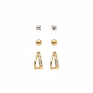 Puede incluir: Un conjunto de tres pares de pendientes dorados. Los pares incluyen dos pendientes de botón redondos con piedras transparentes, dos pequeños pendientes de bola dorados y dos pendientes de aro dorados con piedras transparentes.