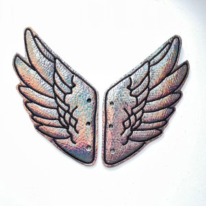 May include: A pair of iridescent silver wings with black stitching, designed to be attached to shoes. The wings have a textured surface and are shaped like angel wings.