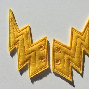 May include: Two yellow felt lightning bolt patches with stitched edges and two holes each.