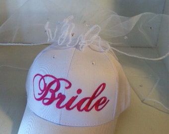 May include: White baseball cap with a pink embroidered "Bride" on the front and a white tulle veil attached to the top.