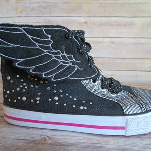 May include: Black high-top sneakers with a sparkly silver toe and a black felt wing attached to the top. The sneakers have a white sole with a pink stripe.