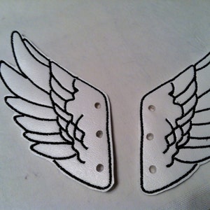 May include: A pair of white fabric shoe laces with black embroidered angel wings. The laces have five holes on each side.