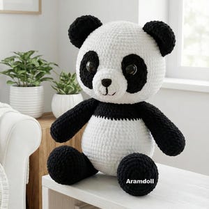 5 ALT TEXT FOR PHOTOS
1) Crochet panda plush sitting on a cozy chair with black ears, black eye patches, and a white face in a neutral room
2) Close-up of amigurumi panda face showing shiny eyes, black eye patches, and a small embroidered smile
3) Full view of crochet panda bear with round belly and chunky black arms and legs posed indoors
4) Side angle of crocheted panda plush highlighting the rounded head, ears, and smooth black-and-white stitch texture