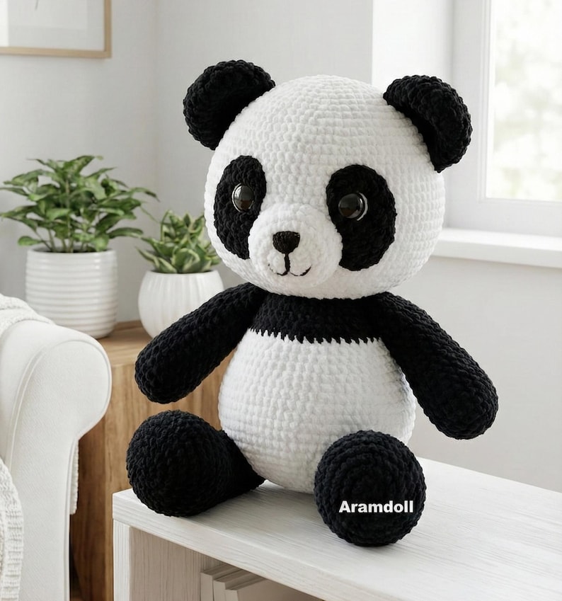 5 ALT TEXT FOR PHOTOS
1) Crochet panda plush sitting on a cozy chair with black ears, black eye patches, and a white face in a neutral room
2) Close-up of amigurumi panda face showing shiny eyes, black eye patches, and a small embroidered smile
3) Full view of crochet panda bear with round belly and chunky black arms and legs posed indoors
4) Side angle of crocheted panda plush highlighting the rounded head, ears, and smooth black-and-white stitch texture