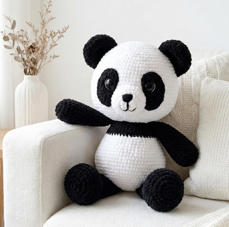 5 ALT TEXT FOR PHOTOS
1) Crochet panda plush sitting on a cozy chair with black ears, black eye patches, and a white face in a neutral room
2) Close-up of amigurumi panda face showing shiny eyes, black eye patches, and a small embroidered smile
3) Full view of crochet panda bear with round belly and chunky black arms and legs posed indoors
4) Side angle of crocheted panda plush highlighting the rounded head, ears, and smooth black-and-white stitch texture