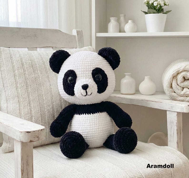5 ALT TEXT FOR PHOTOS
1) Crochet panda plush sitting on a cozy chair with black ears, black eye patches, and a white face in a neutral room
2) Close-up of amigurumi panda face showing shiny eyes, black eye patches, and a small embroidered smile
3) Full view of crochet panda bear with round belly and chunky black arms and legs posed indoors
4) Side angle of crocheted panda plush highlighting the rounded head, ears, and smooth black-and-white stitch texture