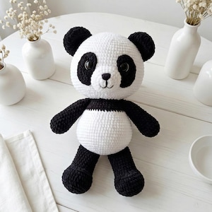 5 ALT TEXT FOR PHOTOS
1) Crochet panda plush sitting on a cozy chair with black ears, black eye patches, and a white face in a neutral room
2) Close-up of amigurumi panda face showing shiny eyes, black eye patches, and a small embroidered smile
3) Full view of crochet panda bear with round belly and chunky black arms and legs posed indoors
4) Side angle of crocheted panda plush highlighting the rounded head, ears, and smooth black-and-white stitch texture