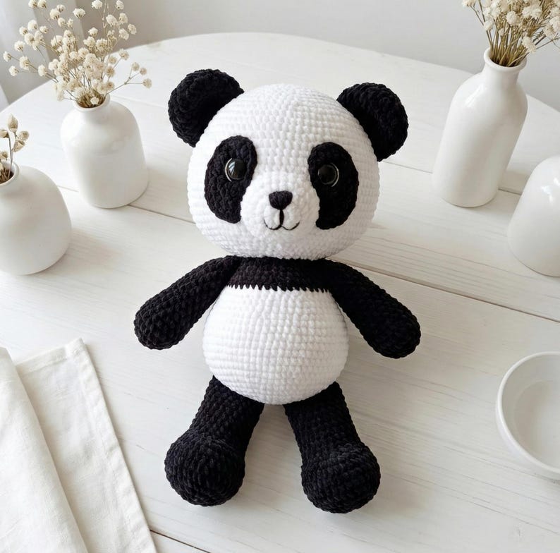 5 ALT TEXT FOR PHOTOS
1) Crochet panda plush sitting on a cozy chair with black ears, black eye patches, and a white face in a neutral room
2) Close-up of amigurumi panda face showing shiny eyes, black eye patches, and a small embroidered smile
3) Full view of crochet panda bear with round belly and chunky black arms and legs posed indoors
4) Side angle of crocheted panda plush highlighting the rounded head, ears, and smooth black-and-white stitch texture