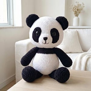 5 ALT TEXT FOR PHOTOS
1) Crochet panda plush sitting on a cozy chair with black ears, black eye patches, and a white face in a neutral room
2) Close-up of amigurumi panda face showing shiny eyes, black eye patches, and a small embroidered smile
3) Full view of crochet panda bear with round belly and chunky black arms and legs posed indoors
4) Side angle of crocheted panda plush highlighting the rounded head, ears, and smooth black-and-white stitch texture