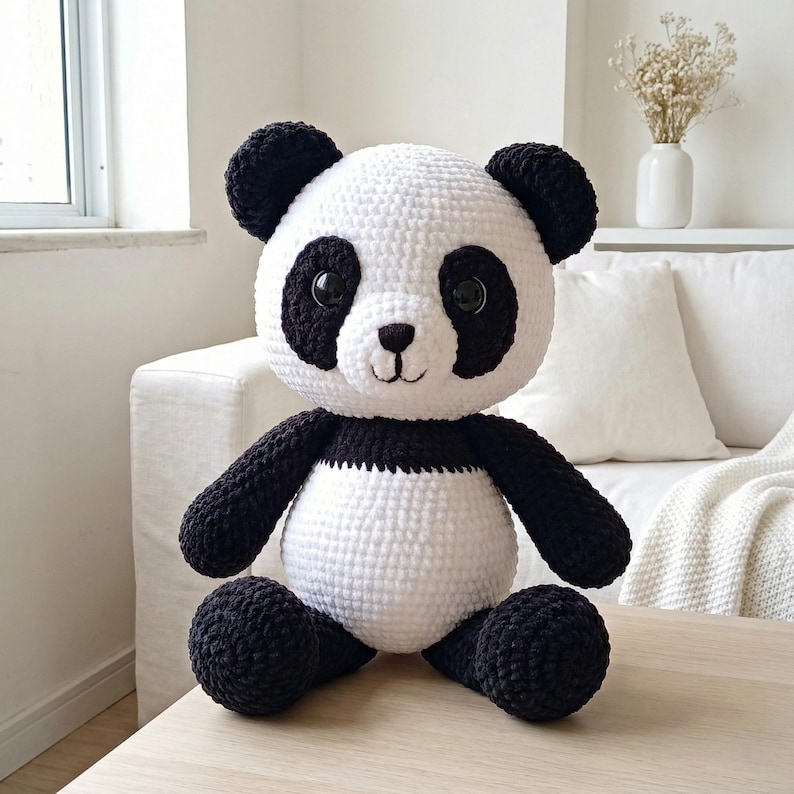 5 ALT TEXT FOR PHOTOS
1) Crochet panda plush sitting on a cozy chair with black ears, black eye patches, and a white face in a neutral room
2) Close-up of amigurumi panda face showing shiny eyes, black eye patches, and a small embroidered smile
3) Full view of crochet panda bear with round belly and chunky black arms and legs posed indoors
4) Side angle of crocheted panda plush highlighting the rounded head, ears, and smooth black-and-white stitch texture