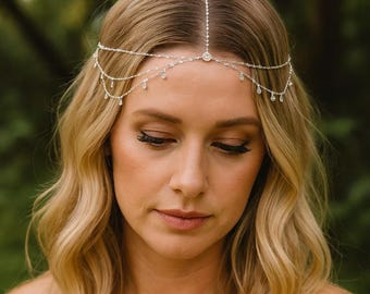 May include: A silver-toned headpiece with a delicate design. The headpiece features a central circular embellishment and multiple strands adorned with small, sparkling crystals. The piece is worn across the forehead and over the hair, adding a touch of elegance.