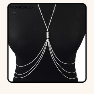 May include: Silver body chain with multiple strands and three pearl accents. The body jewelry is worn over a black top. The brand name "AdorstoreCo" is visible in the top left corner.