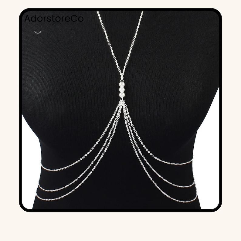 May include: Silver body chain with multiple strands and three pearl accents. The body jewelry is worn over a black top. The brand name "AdorstoreCo" is visible in the top left corner.