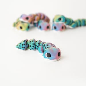 May include: A colorful, segmented caterpillar toy with a gradient of blue, pink, and yellow hues. The toy has black spots and large, black eyes. Several similar toys are in the background, all with the same design.