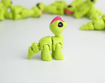 May include: A lime green articulated dinosaur toy with a pink head crest and black eyes. Several similar toys are scattered in the background, all on a white surface. The toy's limbs are jointed, allowing for posing.
