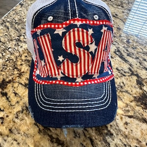 May include: A denim baseball cap with a white mesh back. The front features a red, white, and blue design with the letters "USA" and stars. The brim is distressed, and the cap has white stitching.