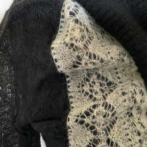 May include: Close-up of a black knit sweater with a white, open-weave lace panel. The lace has a delicate, intricate pattern. The sweater appears soft and textured, with a focus on the contrast between the black and white elements.