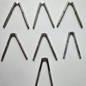 Peut inclure: Un ensemble de sept casse-noix en métal argenté disposés en formation triangulaire. Chaque casse-noix présente une conception articulée avec des poignées texturées et à motifs, ainsi que des extrémités arrondies et des finitions métalliques.