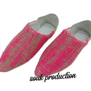 May include: A pair of pink and tan woven slippers with a white interior and gray trim. The slippers are displayed on a white background. The text "souk production" is written in black cursive.