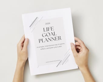 Może przedstawiać: Biały Life Goal Planner na rok 2026, trzymany w dłoniach. Planer zawiera tytuł "LIFE GOAL PLANNER" dużymi, pogrubionymi literami, z tekstem "A simple, intentional way to grow, reflect, and plan your year" poniżej. Szare, ukośne linie akcentują projekt.