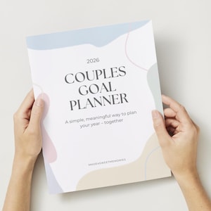Op de afbeelding: Een witte Couples Goal Planner voor 2026, vastgehouden door handen. De omslag heeft pastelkleurige abstracte vormen en de tekst "Couples Goal Planner". De slogan van de planner luidt: "Een eenvoudige, zinvolle manier om je jaar te plannen - samen."