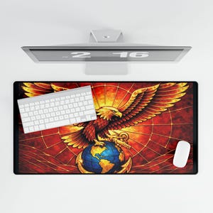 Puede incluir: Alfombrilla de escritorio rectangular con un diseño de vidriera que muestra un águila marrón y dorada agarrando un globo terráqueo. El águila se encuentra sobre un fondo rojo y naranja. Un teclado y un ratón blancos están sobre la alfombrilla.