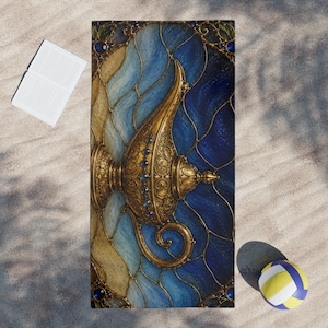 May include: A rectangular beach towel featuring a central ornate gold oil lamp design with intricate filigree and blue gemstone accents. The background displays a stained glass pattern in shades of deep blue, light blue, and cream with dark outlines.