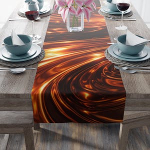 May include: A table runner with a swirling, abstract design in shades of brown and gold. The runner is placed on a wooden table set for a meal, with plates, bowls, silverware, and wine glasses. A vase of pink flowers is in the center.