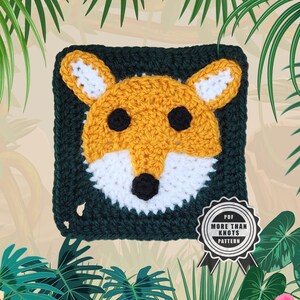Könnte beinhalten: Ein gehäkeltes Fuchgesicht mit orangefarbenen, weißen und schwarzen Details auf einem dunkelgrünen Quadrat. Das Bild enthält ein Abzeichen mit der Aufschrift "PDF MORE THAN KNOTS PATTERN". Das Fuchsmotiv ist von einem dunkelgrünen Rand umgeben.