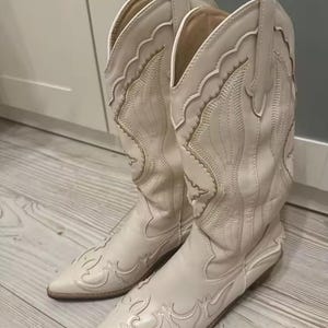 Step into the season with the ultimate statement piece. Our White Vintage Western Boots blend the rugged spirit of the frontier with high-fashion elegance. Featuring intricate tonal embroidery and a sophisticated pointed toe, these knee-high boots are designed to turn heads at weddings, festivals, or on a casual autumn stroll.