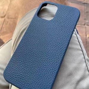May include: A textured, blue phone case. The case has a rectangular shape with rounded edges and a cutout for the camera. The case is made of a material that has a pebbled texture.