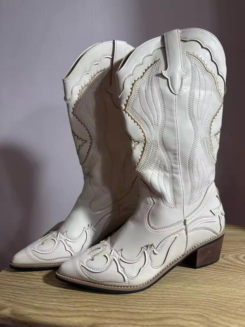 Step into the season with the ultimate statement piece. Our White Vintage Western Boots blend the rugged spirit of the frontier with high-fashion elegance. Featuring intricate tonal embroidery and a sophisticated pointed toe, these knee-high boots are designed to turn heads at weddings, festivals, or on a casual autumn stroll.