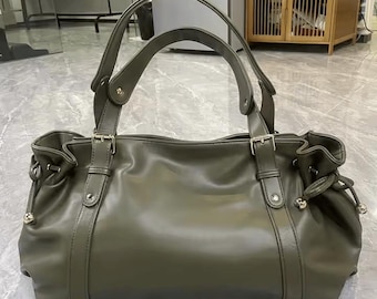 May include: Olive green leather handbag with double handles and silver-tone hardware. The bag features a structured design with a gathered top and adjustable side details. A classic tote style.