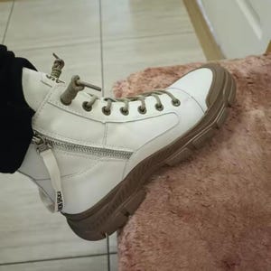 Könnte beinhalten: Weißer High-Top-Stiefel mit brauner Sohle und Zierleisten. Der Stiefel hat einen seitlichen Reißverschluss und eine Schnürung. Die Sohle ist dick und strukturiert. Der Text "FASHION SHOES" ist auf dem Reißverschlussanhänger zu sehen.