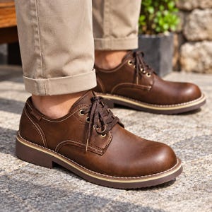 Puede incluir: Un par de zapatos de cordones color marrón oscuro con puntera redondeada, costuras a tono y una suela gruesa de varias capas con una franja clara. Los zapatos tienen ojales metálicos para los cordones oscuros y una pequeña etiqueta.