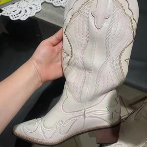 Step into the season with the ultimate statement piece. Our White Vintage Western Boots blend the rugged spirit of the frontier with high-fashion elegance. Featuring intricate tonal embroidery and a sophisticated pointed toe, these knee-high boots are designed to turn heads at weddings, festivals, or on a casual autumn stroll.