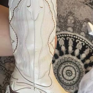 Step into the season with the ultimate statement piece. Our White Vintage Western Boots blend the rugged spirit of the frontier with high-fashion elegance. Featuring intricate tonal embroidery and a sophisticated pointed toe, these knee-high boots are designed to turn heads at weddings, festivals, or on a casual autumn stroll.