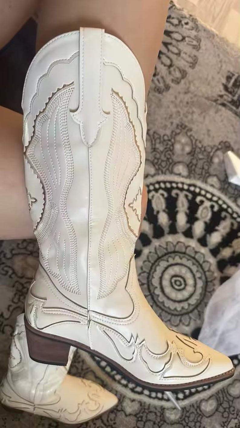 Step into the season with the ultimate statement piece. Our White Vintage Western Boots blend the rugged spirit of the frontier with high-fashion elegance. Featuring intricate tonal embroidery and a sophisticated pointed toe, these knee-high boots are designed to turn heads at weddings, festivals, or on a casual autumn stroll.