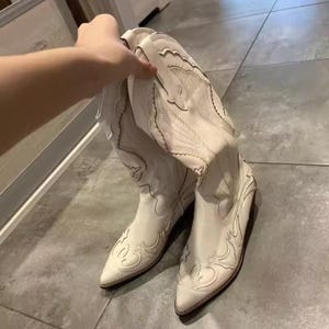 Step into the season with the ultimate statement piece. Our White Vintage Western Boots blend the rugged spirit of the frontier with high-fashion elegance. Featuring intricate tonal embroidery and a sophisticated pointed toe, these knee-high boots are designed to turn heads at weddings, festivals, or on a casual autumn stroll.