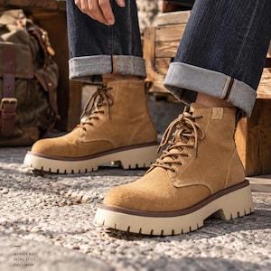 Puede incluir: Un par de botines de ante color tostado con cordones y una suela gruesa de color crema con tacos profundos. Las botas tienen cordones a juego, punta redondeada y un pequeño detalle cosido en la parte superior del cuello. El diseño es sencillo.