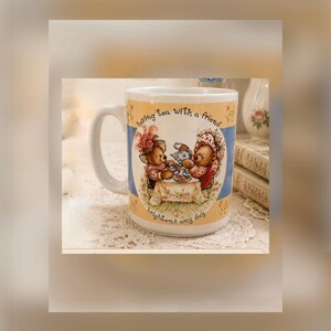 May include: A white ceramic mug featuring a circular illustration of two teddy bears having tea at a table. The text "having tea with a friend" is printed above the bears, and "brightens any day" is printed below. The mug has a blue and yellow border.