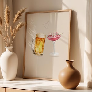 Puede incluir: Una impresión en acuarela enmarcada que presenta una jarra de cerveza y una copa de cóctel. La jarra de cerveza está llena de líquido dorado, y la copa de cóctel está llena de una bebida rosa y cubierta con flores. Un corazón está dibujado encima de las bebidas.