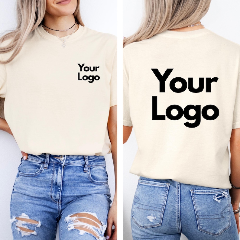 May include: Cream-colored t-shirt with the text "Your Logo" printed in black on the front and back. The shirt is paired with blue denim jeans. The t-shirt has a crew neck and short sleeves.