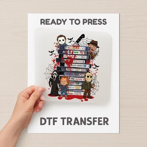 May include: DTF transfer showing a stack of VHS tapes with horror movie titles and cartoon characters such as Michael Myers, Freddy Krueger, and Jason Voorhees. The image includes the text "READY TO PRESS" and "DTF TRANSFER".