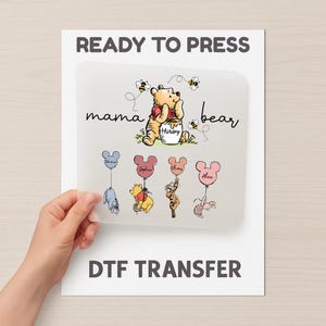 May include: A DTF transfer sheet with the words "READY TO PRESS" and "DTF TRANSFER". The design features Winnie the Pooh as a "mama bear" with bees, and character balloons with names.
