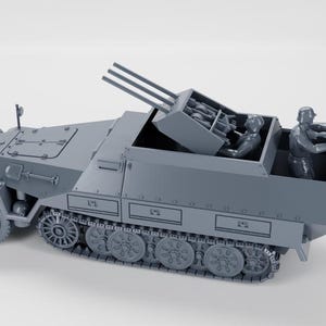 May include: A grey model of a military vehicle with a multi-barrelled anti-aircraft gun. The vehicle has a tracked base and a detailed exterior, including wheels, hatches, and figures of soldiers. The model is set against a plain white background.
